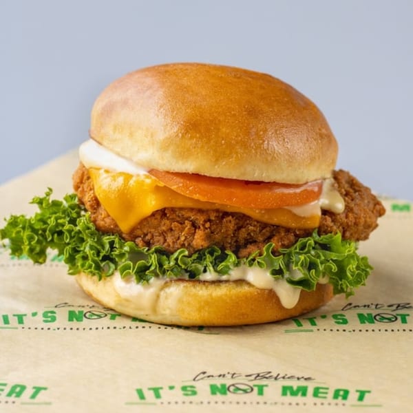 Vegan fried chicken sandwich with lettuce, tomato, cheese, and sauce on a bun.