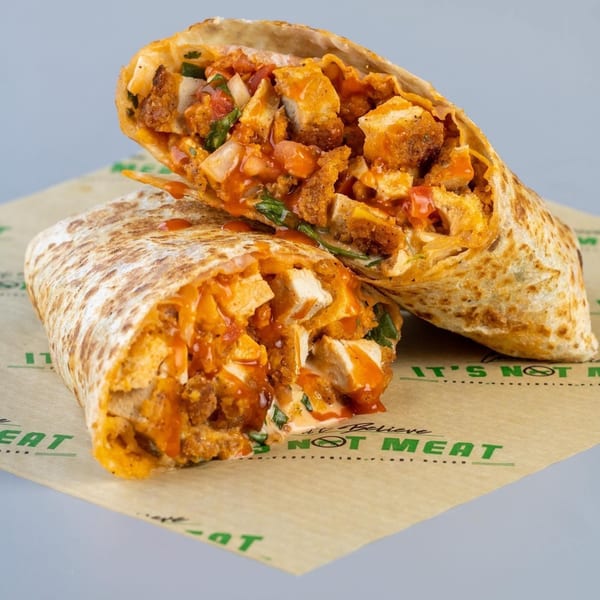 A vegan buffalo chicken burrito, cut in half, revealing plant-based chicken, sauce, and vegetables.