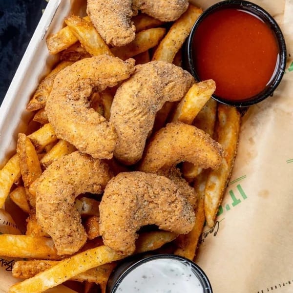 Vegan fried shrimp and french fries with red and white dipping sauces in a paper-lined container.