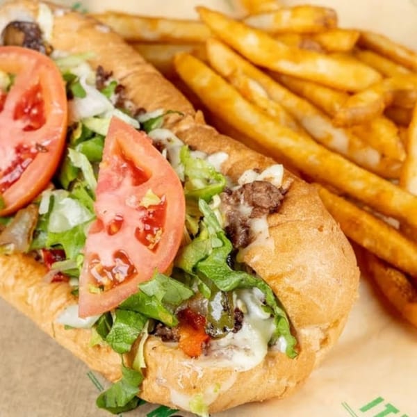 Vegan cheesesteak sub with lettuce, tomato, and fries on a brown paper liner.
