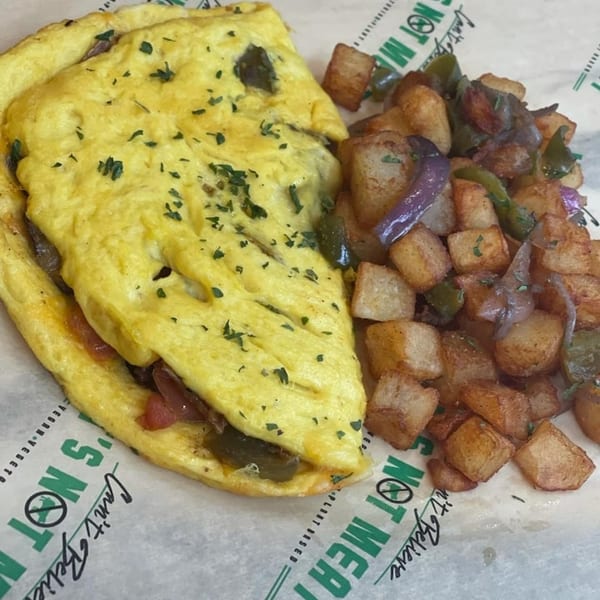 Vegan omelet with herbs, filled with vegetables, served with a side of crispy home fries.