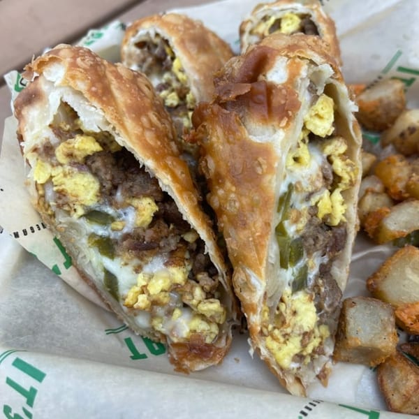 Vegan breakfast burritos, cut in half, filled with scrambled eggs, sausage, and peppers, served with potatoes.