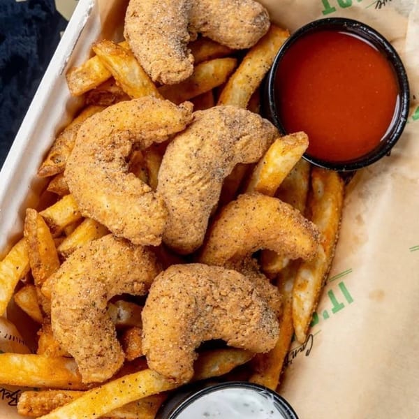 Crispy vegan shrimp and seasoned fries with red and white dipping sauces in a paper-lined basket.