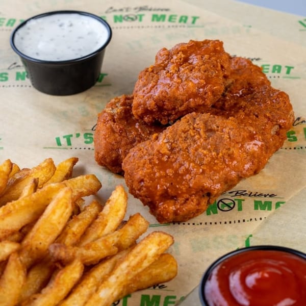 Vegan buffalo wings with fries, ranch, and ketchup on branded parchment paper.