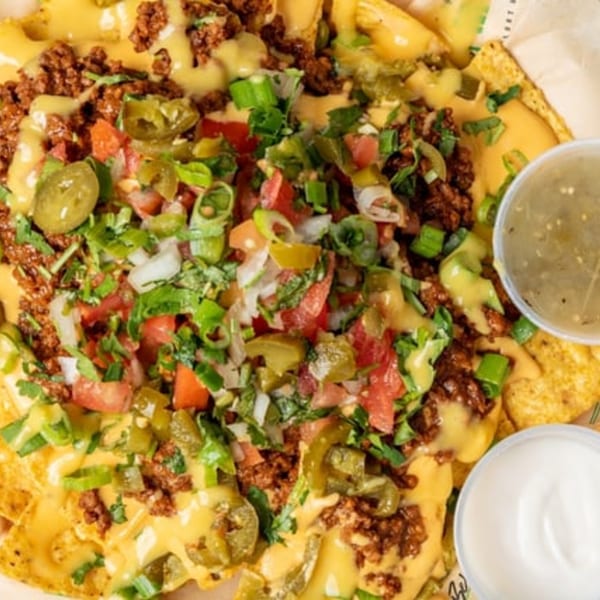 Vegan nachos with plant-based meat, cheese sauce, jalapeños, tomatoes, and green onions.