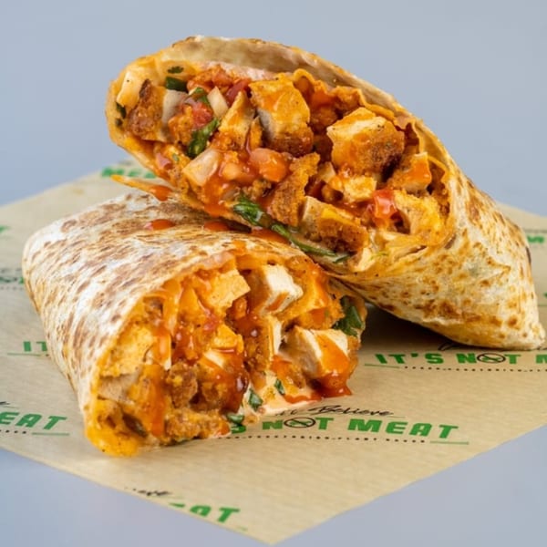 Two halves of a vegan buffalo chicken wrap, filled with plant-based chicken, sauce, and vegetables.