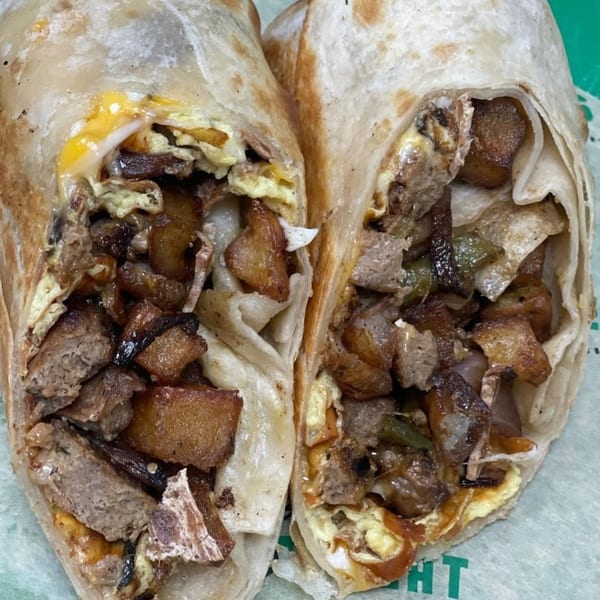 A vegan breakfast burrito, cut in half, revealing plant-based sausage, potatoes, and egg.