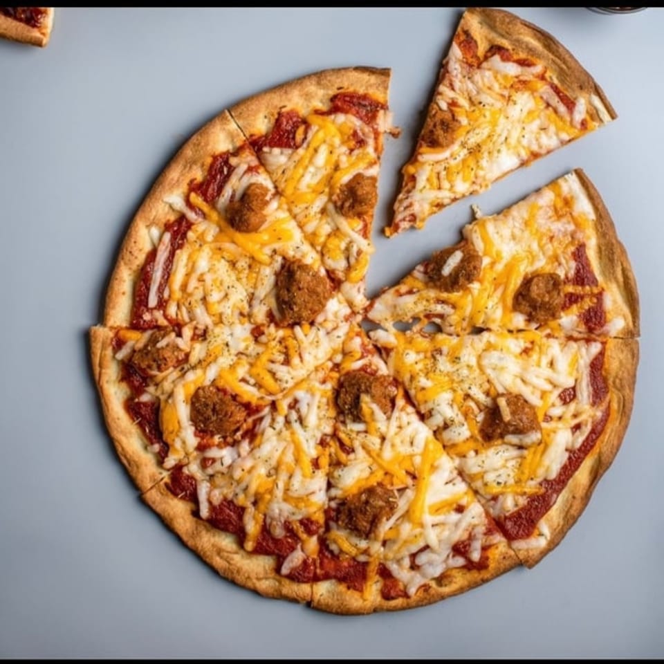 A vegan pizza with tomato sauce, two types of shredded cheese, and meatless meatballs, with one slice removed.