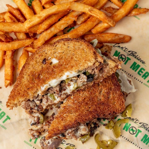 Vegan Philly cheesesteak with melted cheese, peppers, and onions, served with golden fries.